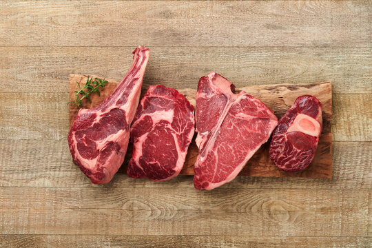 Raw prime steaks. Variety of fresh black angus prime meat steaks T-bone, New York, Ribeye, Striploin, Tomahawk cutting board on old wooden background. Set of various classic steaks. Top view.