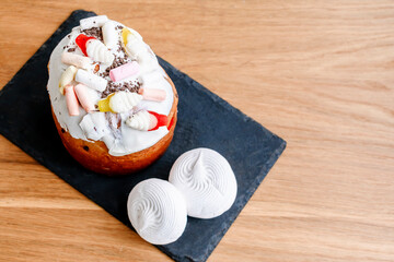 Easter holiday food concept. Homemade Easter cake with white icing, jelly candies, sweet powder, marsmallow, candles, decorated with colored eggs on wooden background with copy space. top view