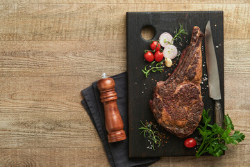 Tomahawk steak. Sliced grilled tomahawk beef steak with baked cherry tomatoes, herbs and salt on old wooden background. Preparing to grill.  Top view and copy space.