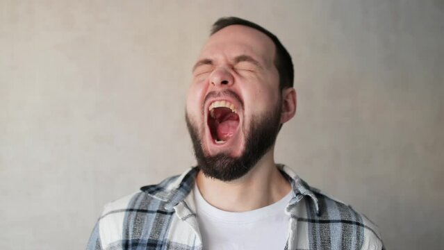 Man yawning and looking at the camera. Bearded handsome man yawns wearily at home