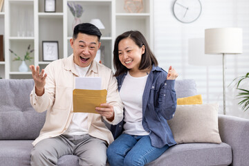 Cheerful and happy asian family together, man and woman at home on sofa sitting in living room, received postal envelope with good news, message and good achievement news. - Powered by Adobe