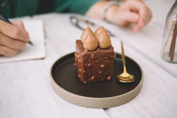 Selective focus on tasty fresh dessert for brunch with buts and chocolate, unrecognizable woman ordered cake for appetizing during cheat meal weekend during time for planning in cafe interior