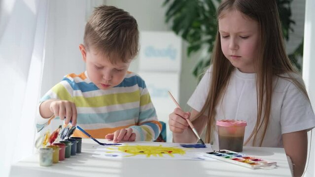 Brother and sister draw a picture with paints on a piece of paper. Children are learning to draw. Home creativity.