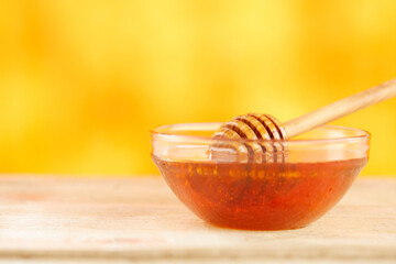 Honey dripping from honey dipper in glass bowl. Close-up. Healthy organic Thick honey dipping from the wooden honey spoon, closeup. jar on the wood table. organic food on color background.