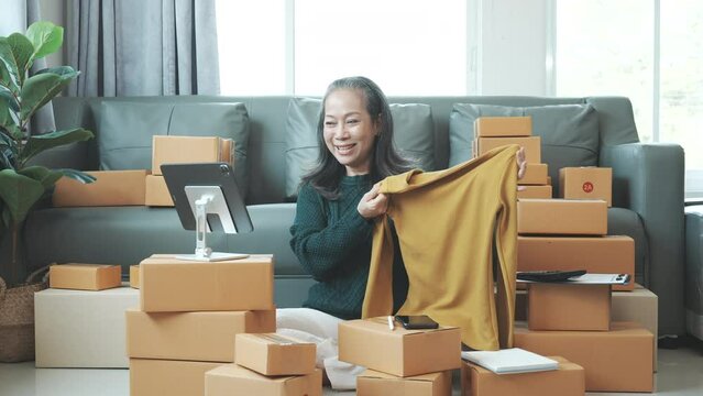 Successful asia people woman entrepreneur with parcel boxes clothing online store checking email order in tablet and laptop at sofa home office SMEs small company.