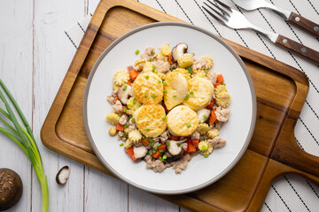Stir fried egg tofu and chicken in oyster sauce with corn, carrot and shiitake in white dish on wooden table.