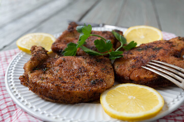 Breaded pork chops with parmesan, parsley crust on a plate with lemon.