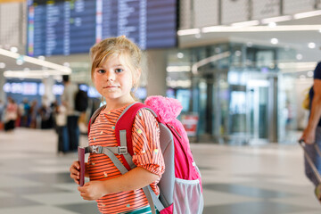 Little preschool girl at airport terminal. Happy child going on vacations by airplane. Smiling kid with passport and bag.