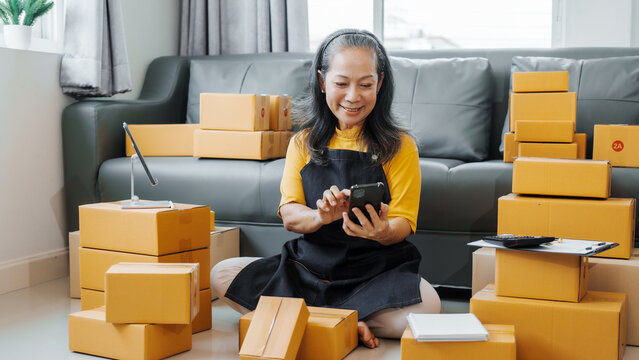 Successful asia people woman entrepreneur with parcel boxes checking email order in tablet and laptop at sofa home office SMEs small company.