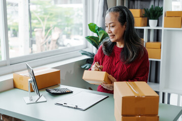 Successful asia people woman entrepreneur with parcel boxes clothing online store checking email order in tablet and laptop at sofa home office SMEs small company.