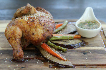Roasted chicken with vegetables and spicy sauce on a wooden plate