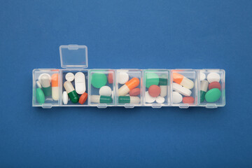 Daily pill box with medications and nutritional supplements on dark blue.