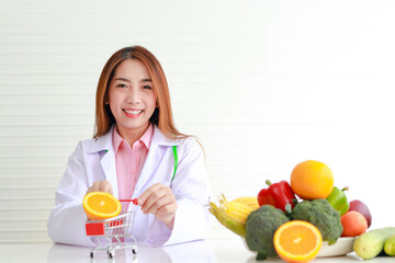 Portrait of a beautiful Asian nutritionist sitting on a white table with fruits and vegetables on the table. healthy food concept