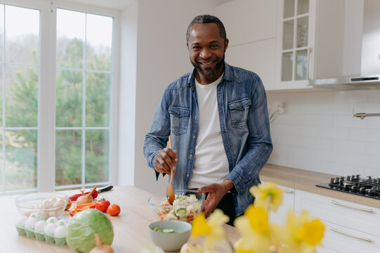 An African American man prepares a vegetable salad. A black man is preparing a dish of vegetables in the kitchen.