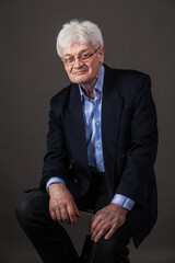 Portrait of an elderly man in a business suit on a dark background. 