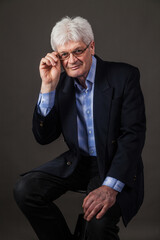 Portrait of an elderly man with glasses and a dark business suit on a dark background. 