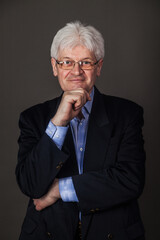 Portrait of an elderly man in glasses and a business suit on a dark background. 