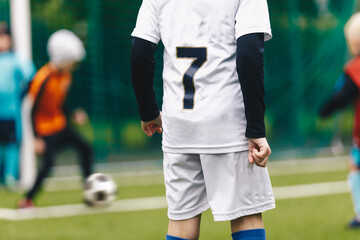 A young boy in a soccer team wearing a white jersey shirt with the number seven on its back. Youth...