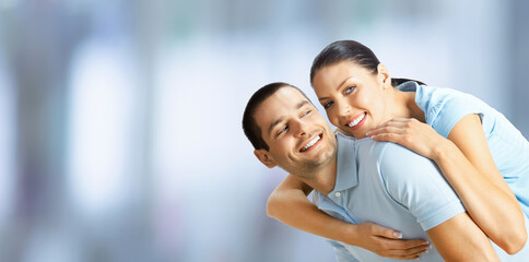 Obraz premium Happy amazed smiling couple. Portrait of standing close embracing, piggyback pose models, indoors. Brunette man and woman together. Copy space text sign area.