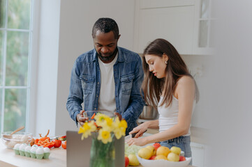 A happy interracial couple preparing food in the kitchen. an African-American man and a Caucasian woman prepare a salad