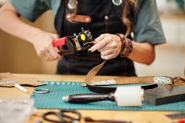 Hands of woman using leather hole rotary punch when working on belt for customer