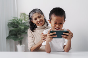 Playing mobile game together, Asian grandson and grandmother people sitting together at desk.