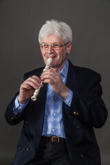 Portrait of an elderly musician in glasses and a dark suit playing a pipe. 