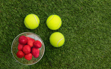 3 Tennis ball and a glass with strawberries on grass.