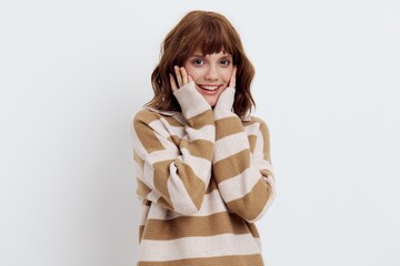 a beautiful, sweet, attractive woman stands in a striped sweater on a light background and gently touches her face with her fingers while looking at the camera. Horizontal photo with empty space