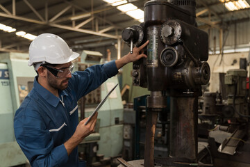Male factory worker maintenance machine in industrial factory, working with digital tablet computer. Male technician inspecting lathe machine. Male engineer repairing machine in workshop