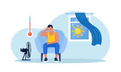 Man chilling on armchair under cooling fan, under blowing air at home. High temperature, hot weather. Summer. Exhausted tired person suffering from heat stroke. Overheating and exhaustion. Dehydration