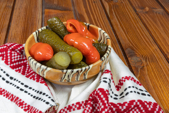 Mixed pickles of cucumbers and red bell peppers. Pickles in Romanian traditional clay bowl on wooden table.