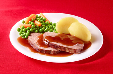 Kasseler mit Kartoffeln Erbsen und Moehren angerichtet auf weissem Teller mit rotem Fond