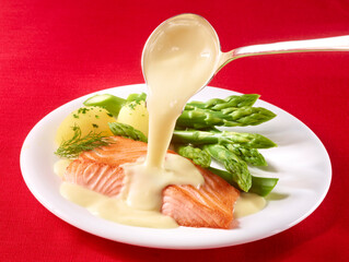 Lachs und Spargel mit Kartoffeln und Hollandaise Sauce auf weissem Teller und rotem Fond