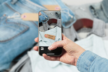 Womans hand taking photo of denim shirt to upload in second hand clothes app