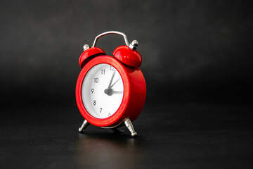 Red bell alarm clock on a dark black background with natural light. Mention of personal care...