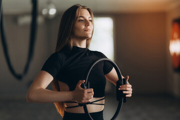 Full-length portrait of a beautiful smiling athletic woman in a black and white tracksuit in a studio, working out with a glute circle. Flexible girl.