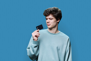 Obraz na płótnie Canvas Young handsome guy holding credit card in hands on blue background