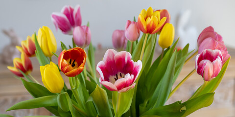 Tulips of different colors in a vase on a table with Easter bunnies in the background