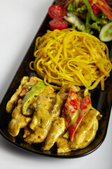 Grilled Chicken with Curry Sauce Linguine Pasta and Green Salad on Black Plate White Background
