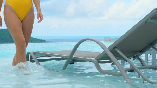 Sexy woman in swimwear lying on lounge chair in poolside on tropical holiday, enjoying the beautiful weather and stunning surroundings of a luxurious resort.