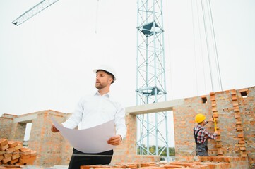 Engineering Consulting People on construction site holding blueprint in his hand. Building inspector. Construction site check drawing and business workflow of new building.