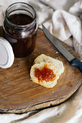 Breakfast of a loaf on top of a chopping board and an open jar of jam and a knife.