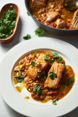 Red Salmon Curry with Tomatoes and Fried Vegetables with a Garnish of Cilantro. Asian Cuisine. Fried salmon with vegetables and green cilantro in white plate. Close up. Vertical photo 