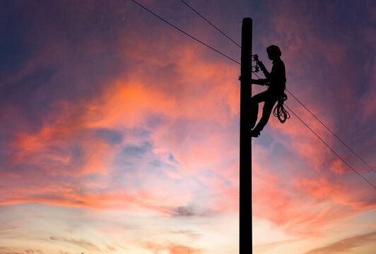 Silhouette of Electrician repairing wire on electric power pole at the sunsetbackground.