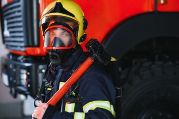 Photo of young fireman with sledgehammer in hands near fire engine