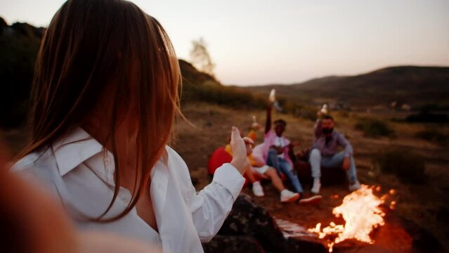 Caucasian woman takes selfie with her friends at camping, they laughing and smiling, hold alcoholic cocktails and drinks their hands. A girl takes pictures of herself friends in outdoor