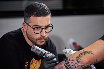 Close up tattoo machine. Tattooing. Man creating picture on his arm by a professional tattoo artist.