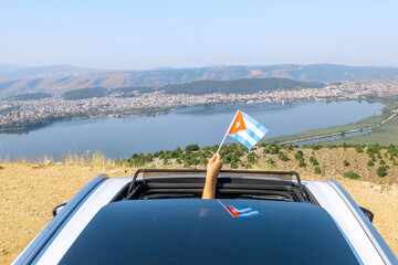 Woman holding Cuba flag from the open car sunroof,  window driving along the serpentine road in the mountains. Top view.  Concept