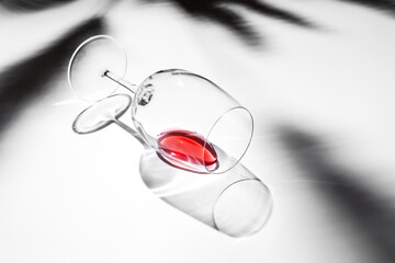 A wine glass lying on white background with a bit of red wine - 588848301